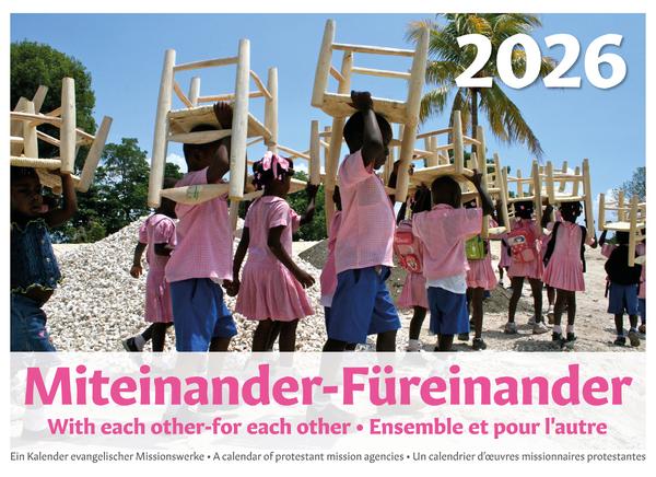 Der Kalender 2026 hat den Titel „Miteinander-Füreinander“ welcher unten auf dem Titelmotiv steht. Auf dem Titelmotiv sieht man das Bild des Monats Juli. Viele Schulkinder in rosafarbener Schuluniform tragen kleine Holzstühle für den Unterricht. Sie gehen auf einem Kiesweg, im Hintergrund sieht man Bäume und Palmen. Das Bild wurde auf Haiti aufgenommen. © Foto: Jürgen Schübelin