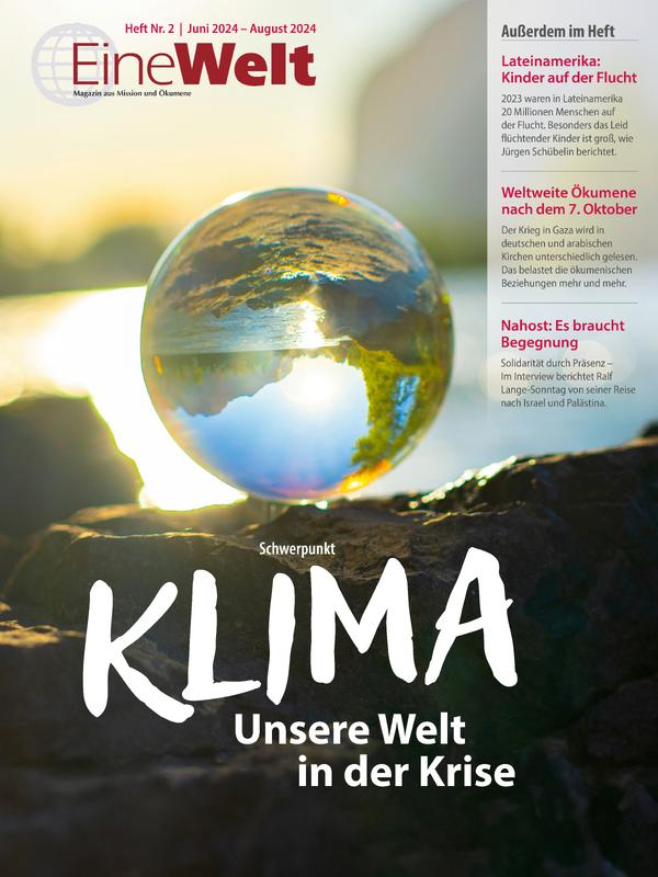 Cover EineWelt 2/24: Eine Glaskugel am Rande eines Sees liegt auf schwarzem Boden. Die Kugel ist scharf, der Rest unscharf. In der Kugel spiegelt sich grüne Natur.© Foto: Alin Andersen/unsplash